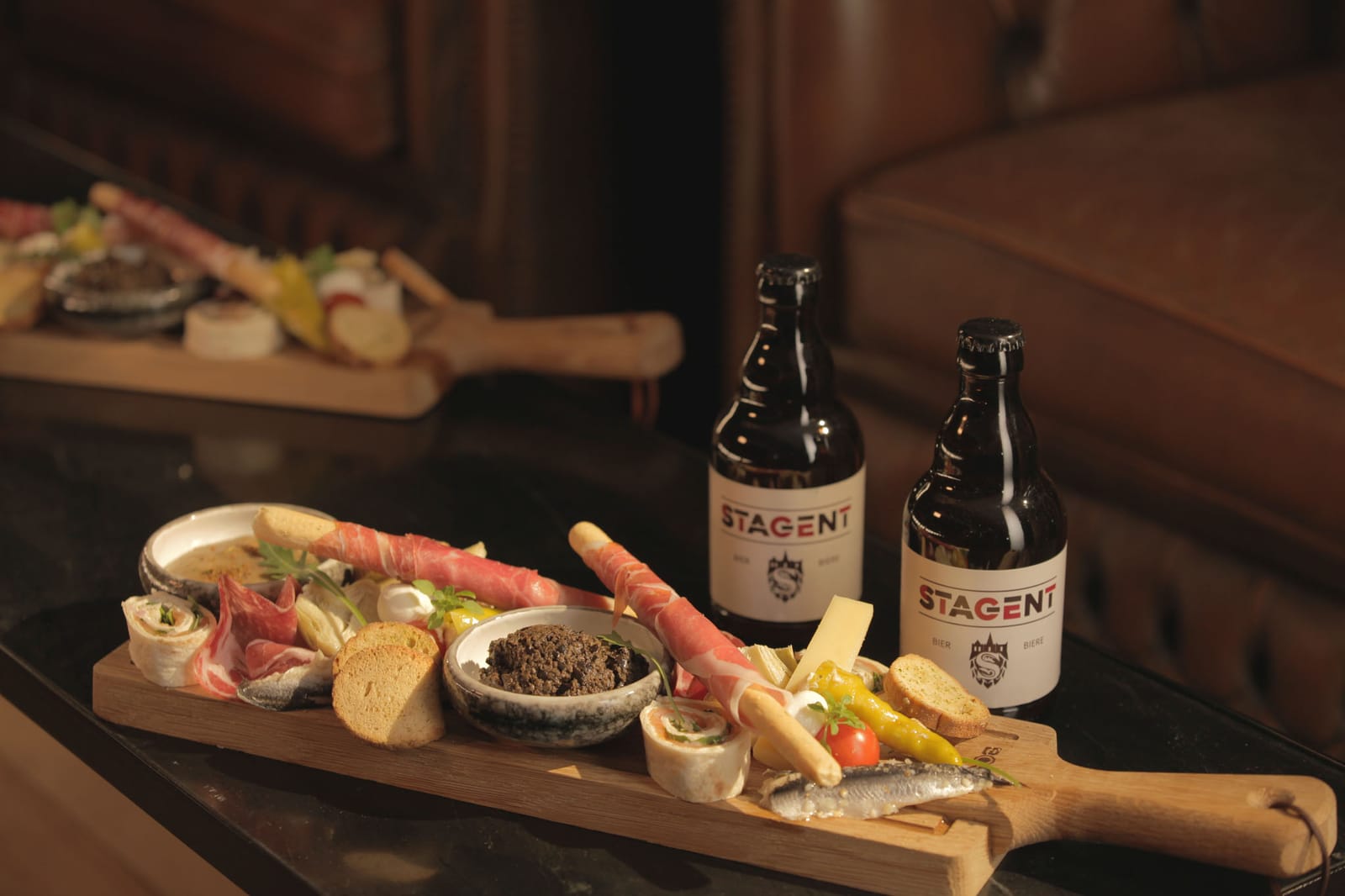 Twee flesjes Stagent op een borrelplank met kaas en charcuterie.